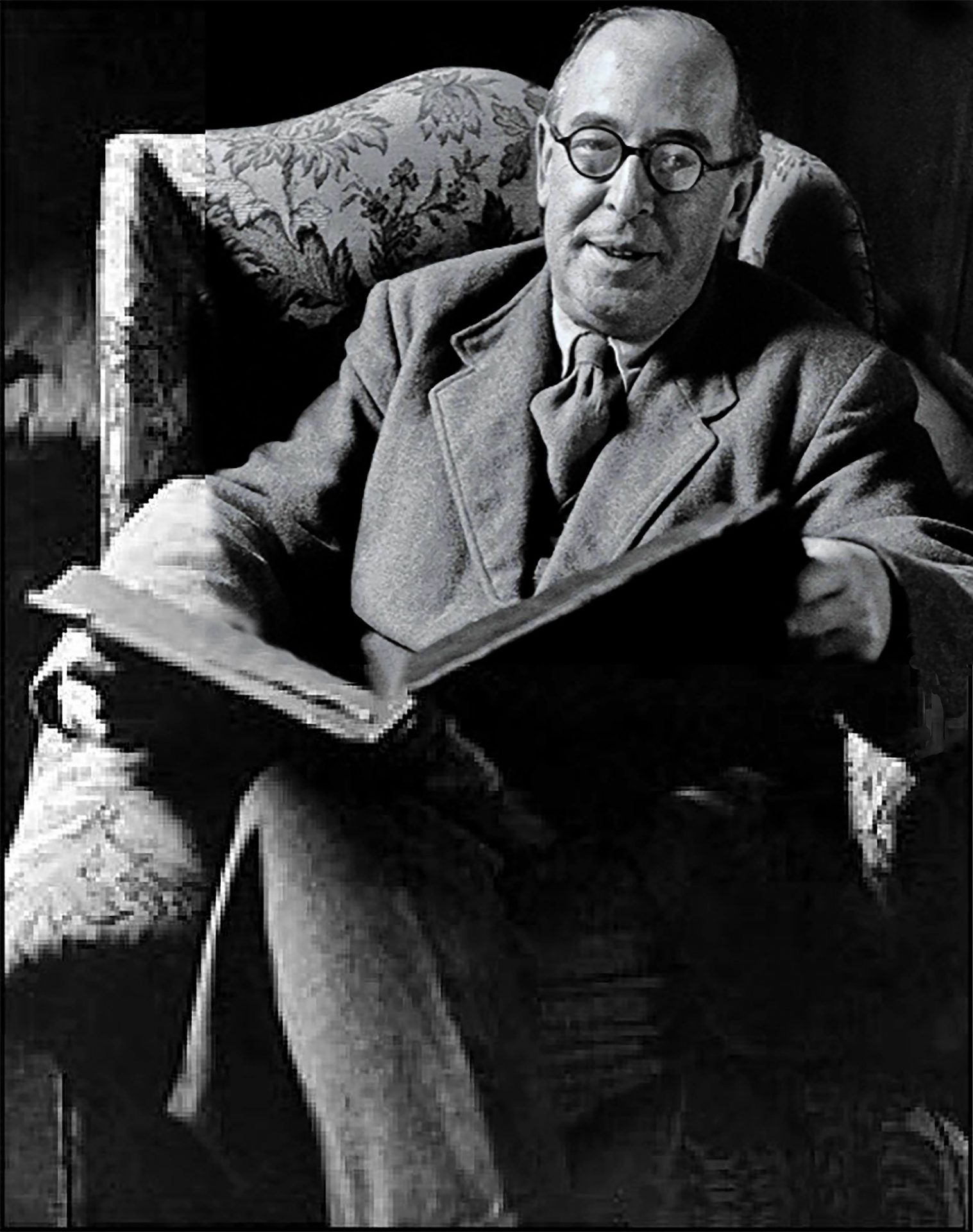 C. S. Lewis sentado numa poltrona, segurando um livro aberto